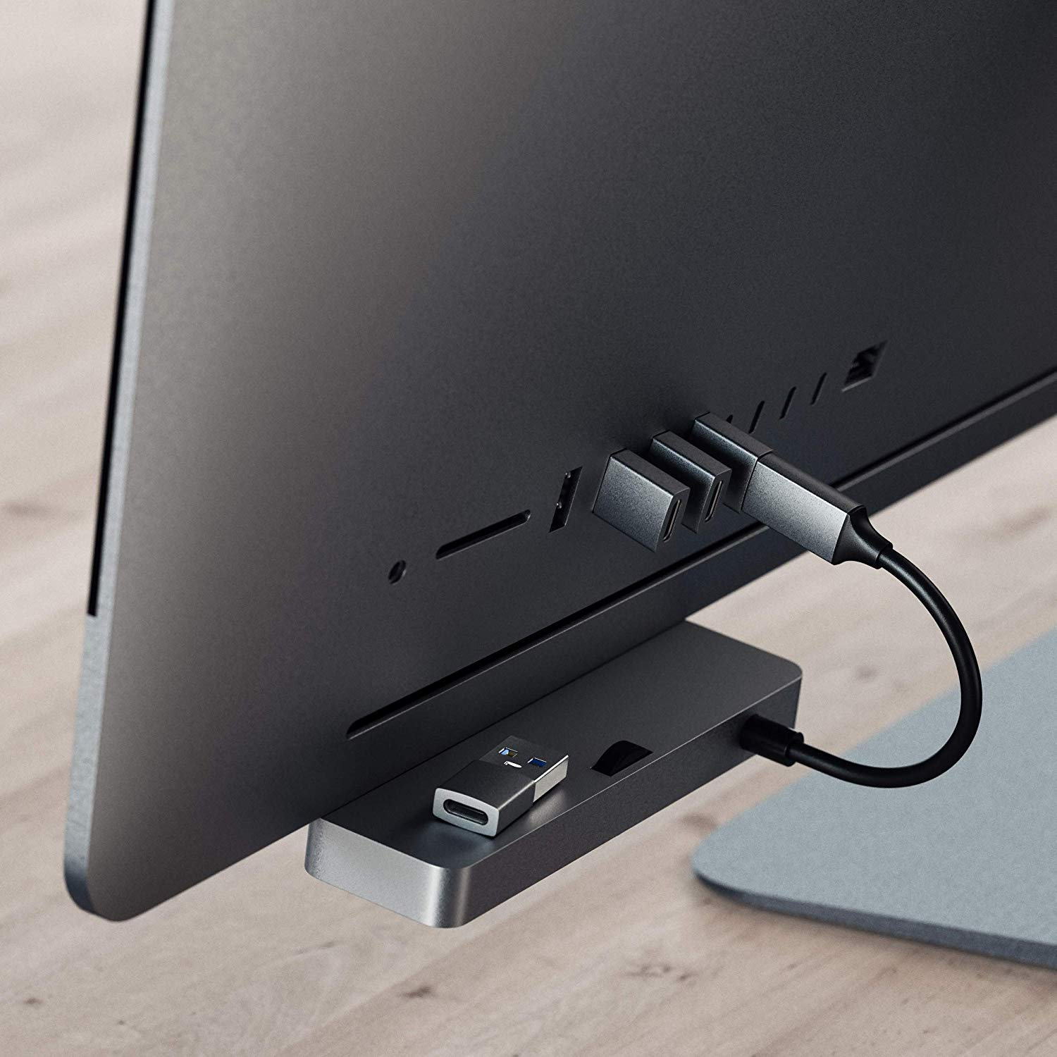 Un écran d'ordinateur avec un hub USB connecté à son dos avec une table en bois grise.