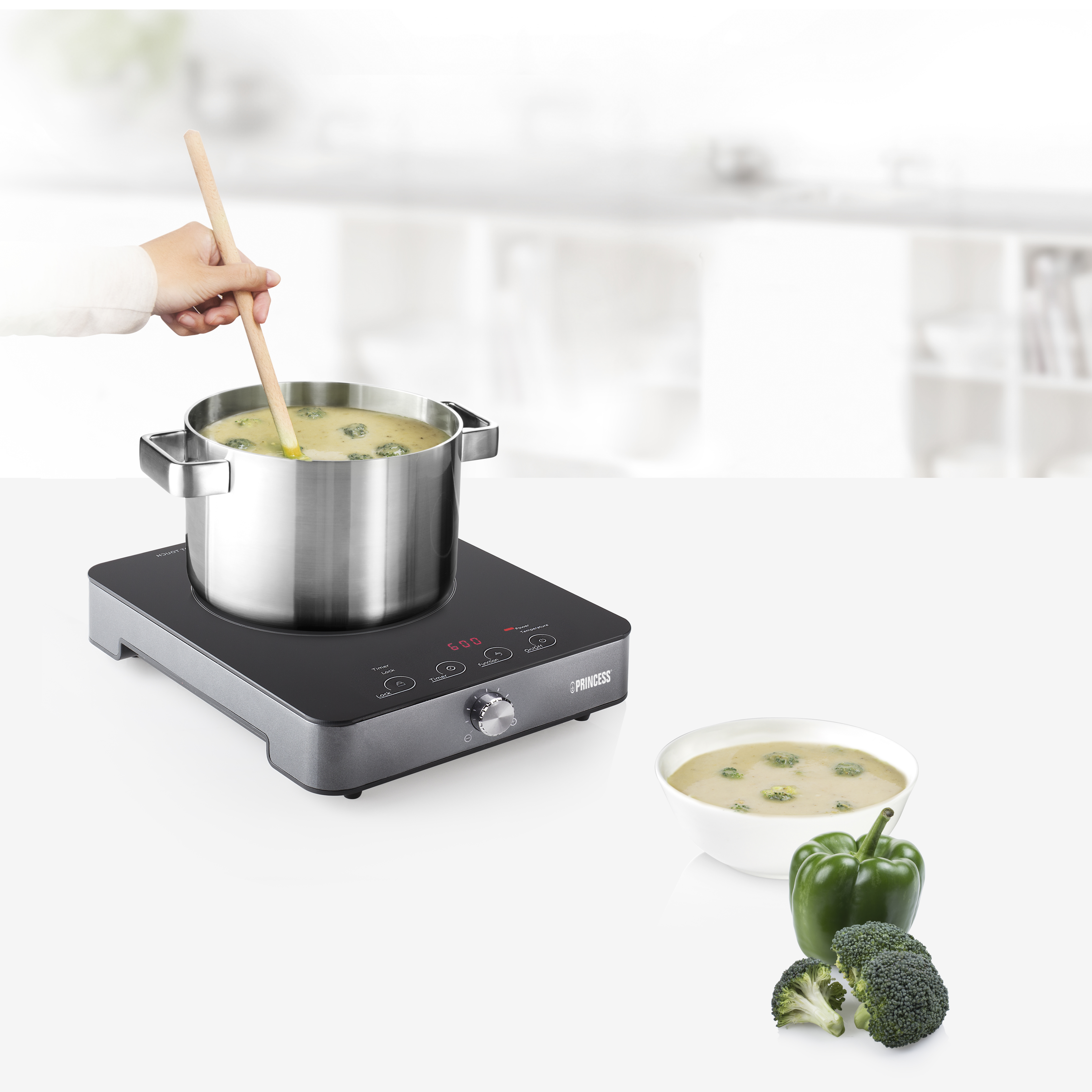 Een pan met broccolisoep op een inductieplaat. Een kom en ingrediënten zijn in de buurt.