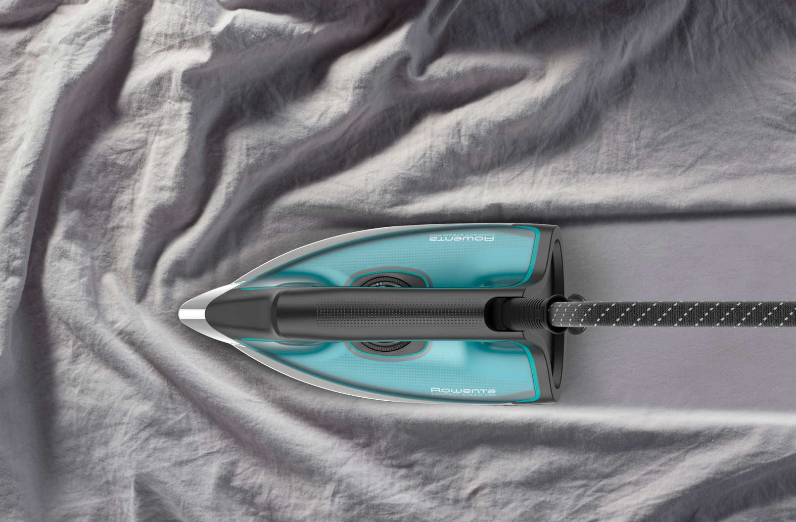 Fer à repasser Rowenta sur tissu gris. Vue de dessus, accents turquoise, poignée noire avec cordon. Traces de vapeur visibles.