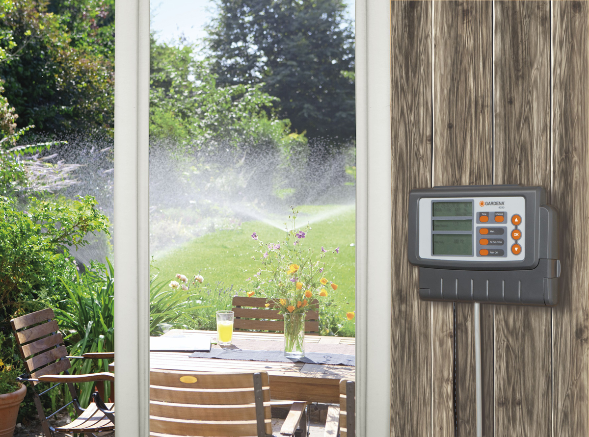 Gartensprinkleranlage, Blick durch ein Fenster. Holzzaun rechts.