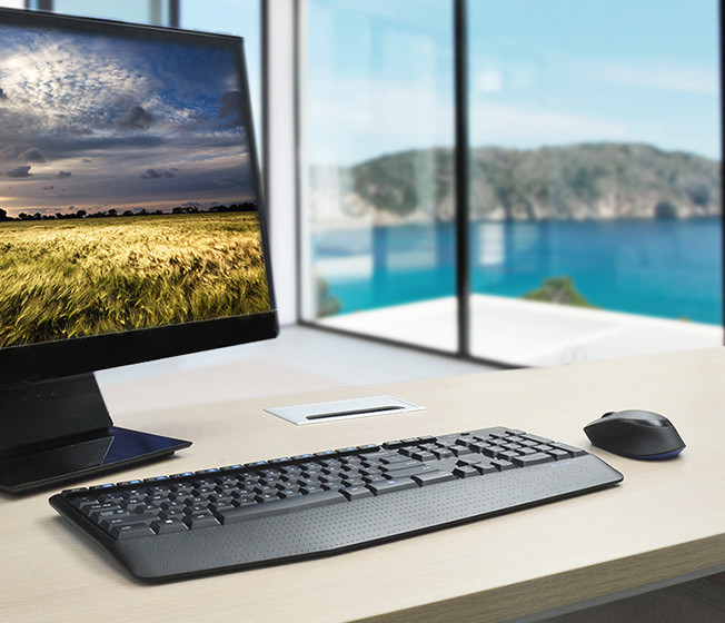A desk with a monitor, keyboard, mouse, and a window with a landscape view.