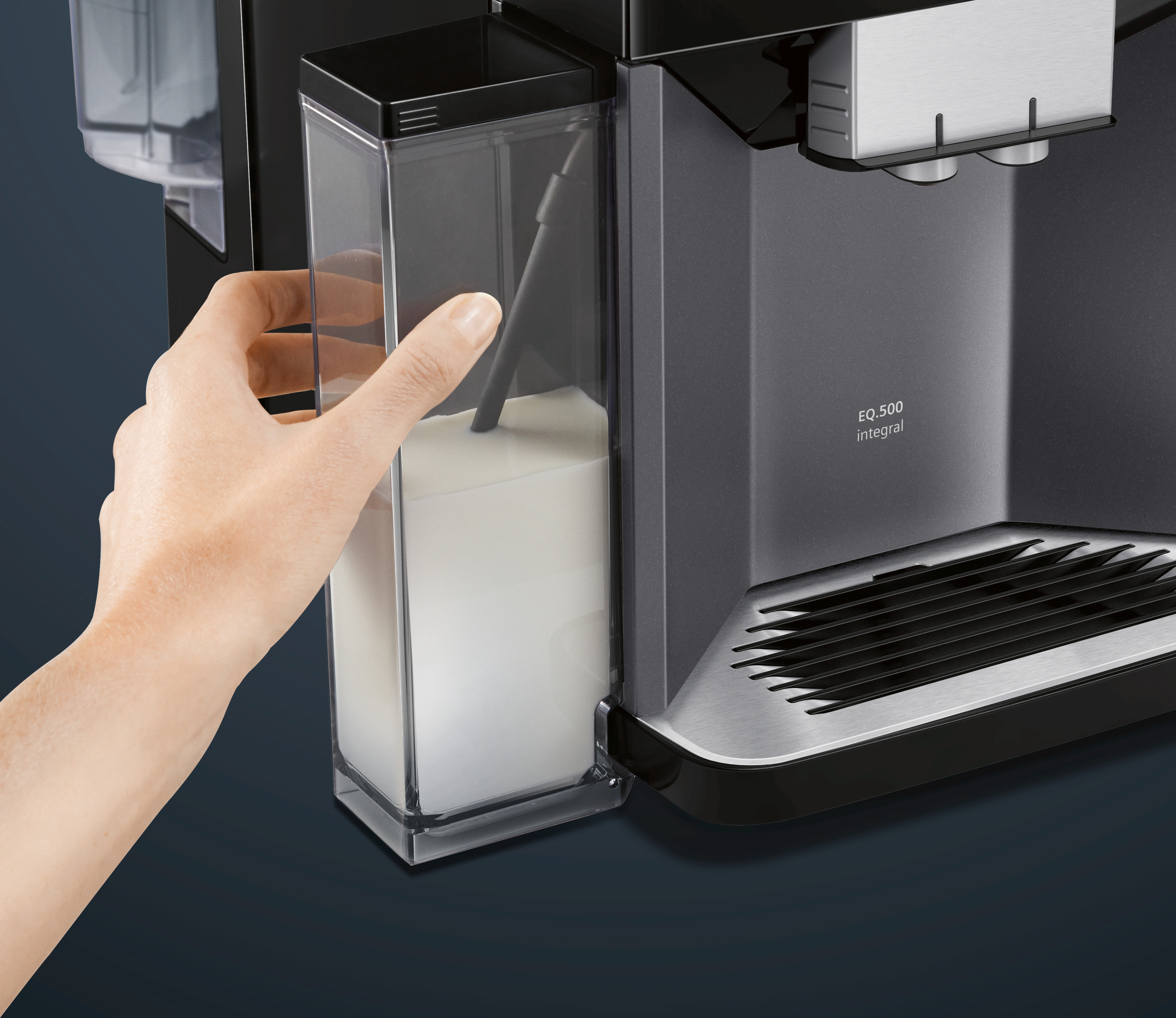 Die Hand einer Person hält einen Milchbehälter in der Nähe einer Kaffeemaschine.