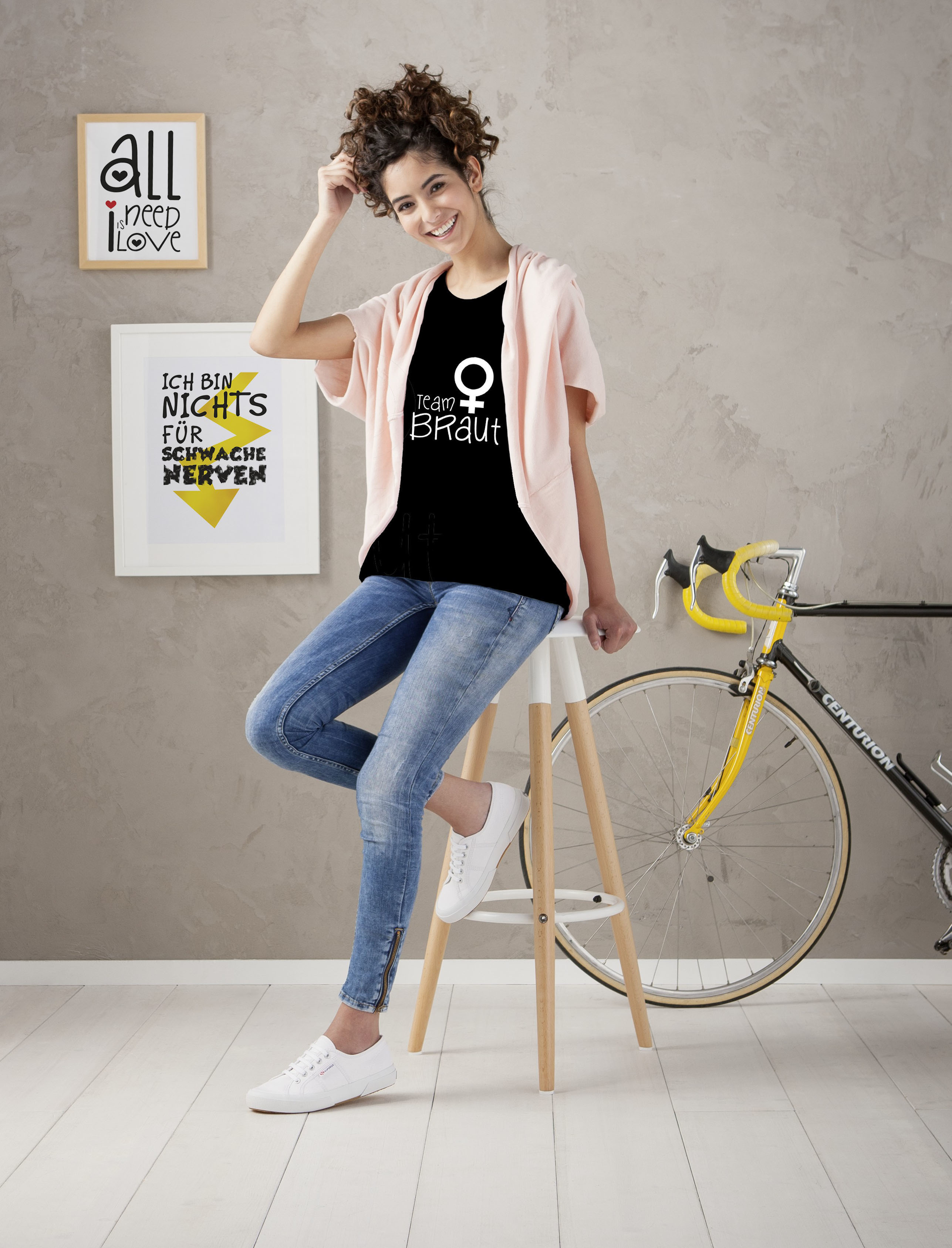 Frau in schwarzem Shirt mit 'I am Braut' und Jeans, neben einem Fahrrad.
