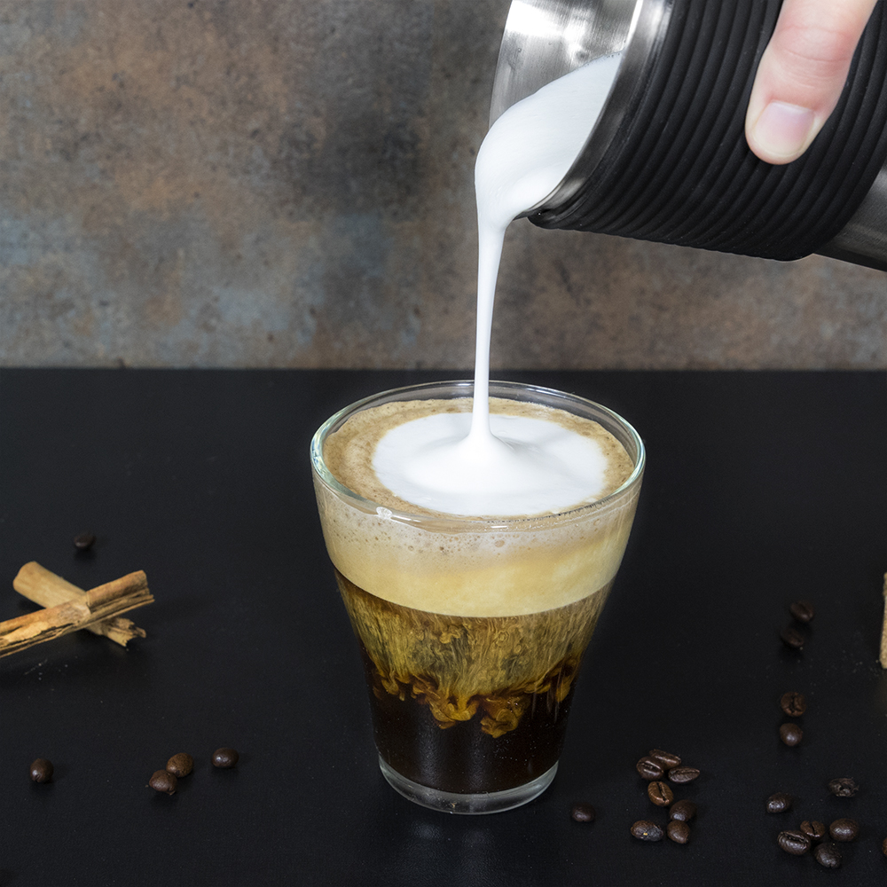 Café que se vierte en un vaso con una capa espumosa.