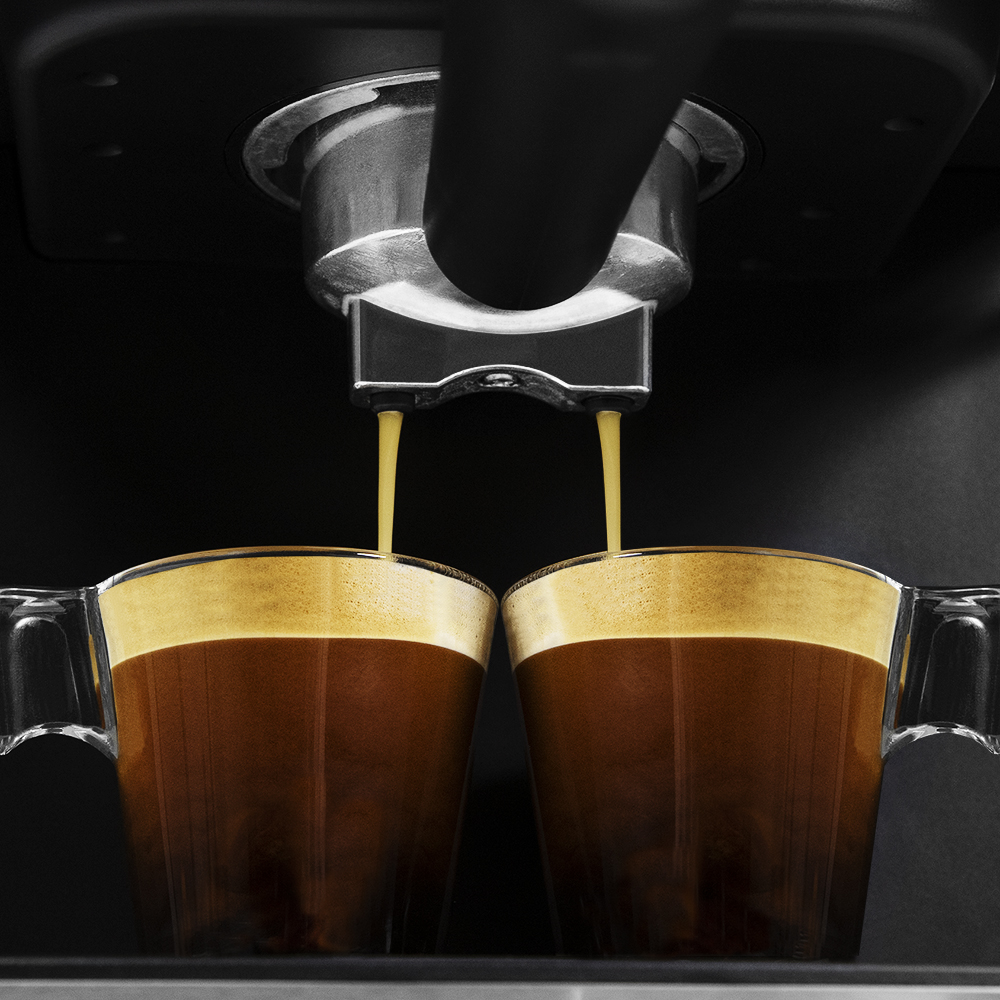 Dos tazas de espresso siendo vertidas desde una máquina de café.