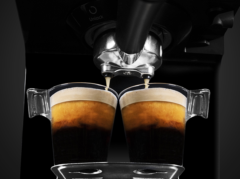 Máquina de espresso dispensando café en dos tazas de vidrio. Café oscuro y rico con crema, sobre fondo negro.