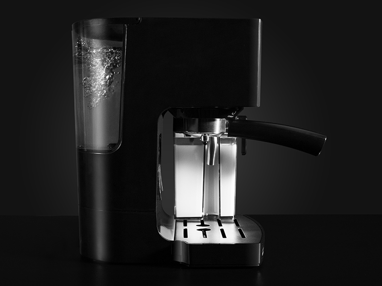 Una máquina de espresso negra y plateada. Tiene un depósito de agua con burbujas, un portafiltro y un mango negro, sobre un fondo oscuro.
