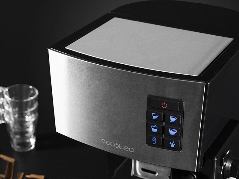 Primer plano de una cafetera de acero inoxidable con botones iluminados. Tazas de vidrio transparente y palitos de canela en el fondo.
