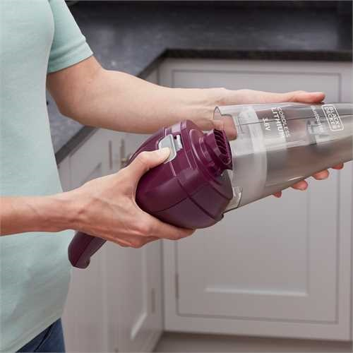 A person's hands assembling a handheld vacuum cleaner, with purple and grey parts.
