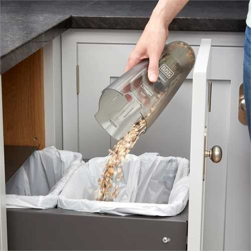 Hand pouring debris from a handheld vacuum into a trash bag.