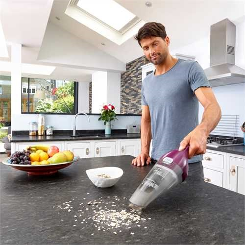 Man vacuums a countertop, scattering crumbs.