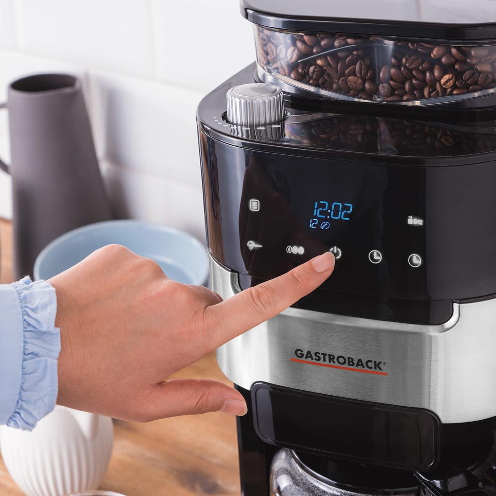 Eine Hand drückt die Einschalttaste auf dem Bedienfeld einer Kaffeemaschine.