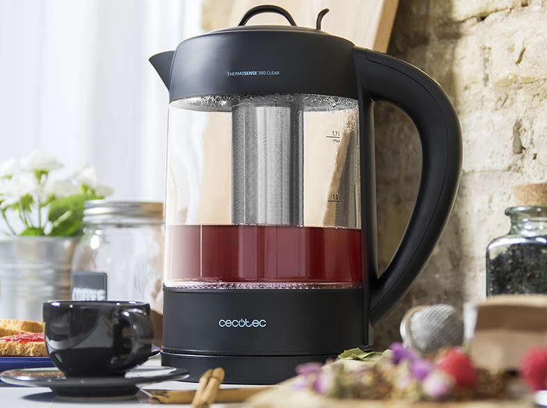 Una tetera eléctrica de vidrio transparente con líquido rojo, hojas de té y una taza negra.