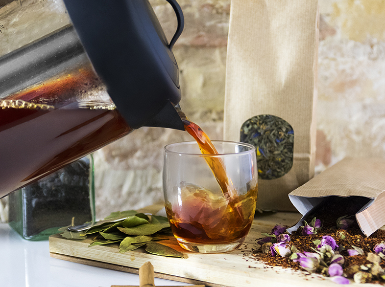 Té vertiéndose en un vaso desde una jarra, con ingredientes y flores.