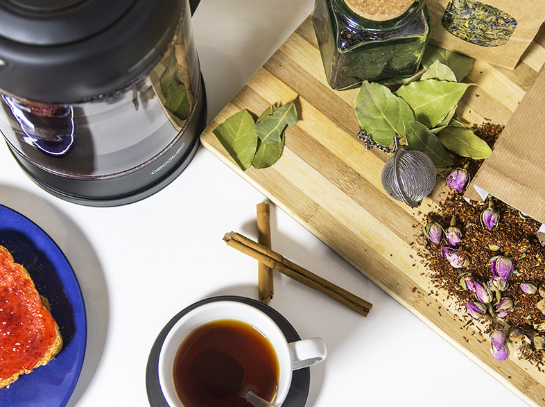 Una mesa con tetera, té, tostadas y varios ingredientes para el té.