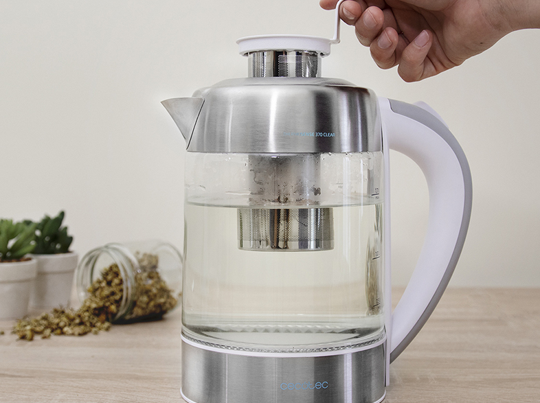 Persona vertiendo agua en una tetera de vidrio con un infusor de té. Otros ingredientes están en la mesa.