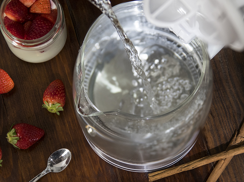 Se vierte agua en una tetera. Fresas y una cuchara sobre la mesa.