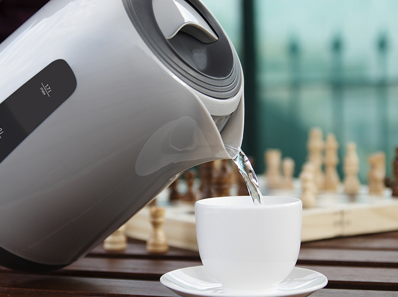 Una tetera vierte agua en una taza de té blanca sobre un platillo. Un tablero de ajedrez está en el fondo.