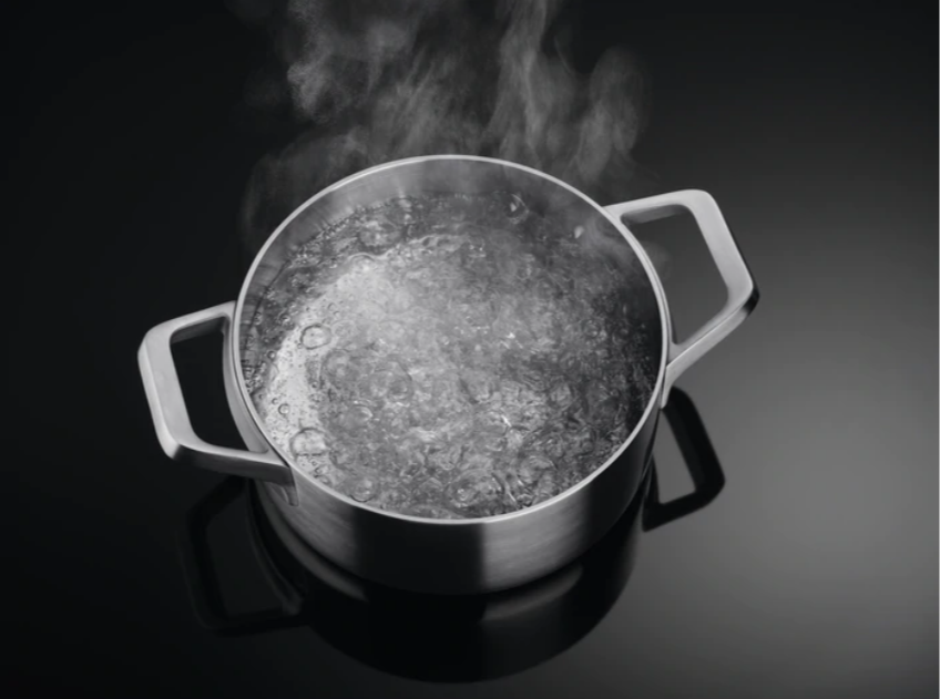 Een roestvrijstalen pan met kokend water en stoom, op een zwart fornuis.