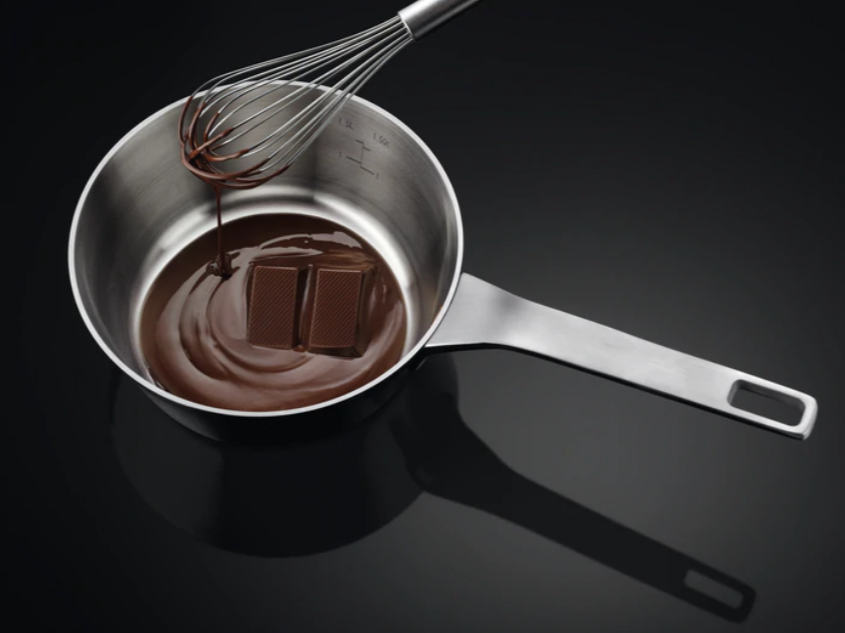 Gesmolten chocolade in een pan met een garde en chocoladeblokjes.