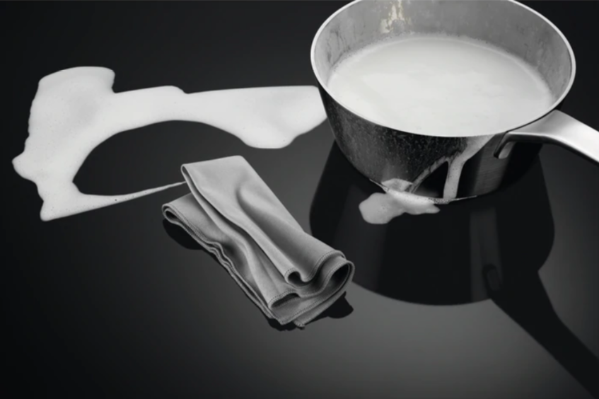 Rvs pan met melk die over een zwart oppervlak stroomt, met een grijze doek.