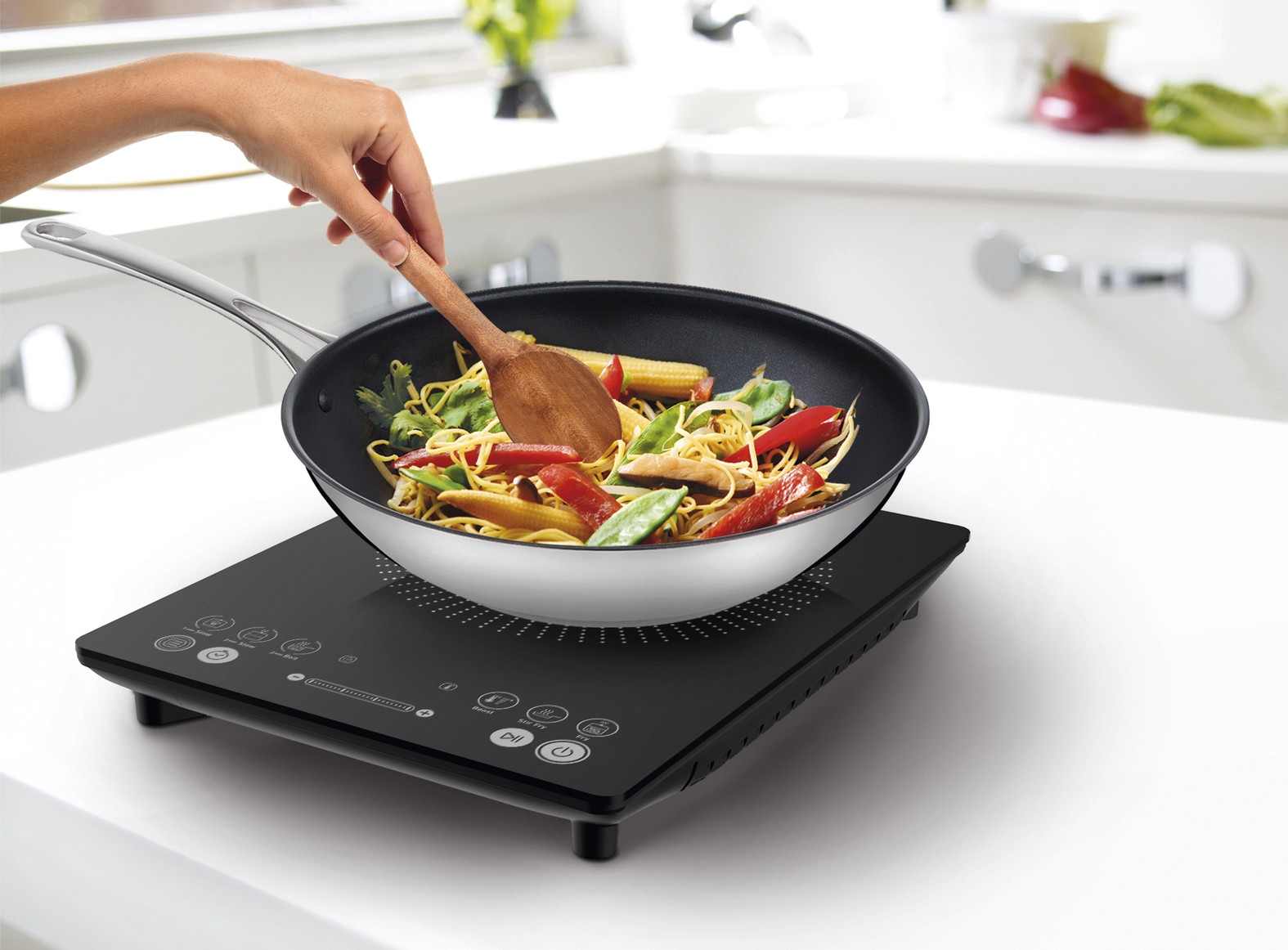 A person cooking noodles in a pan on a portable induction cooktop.