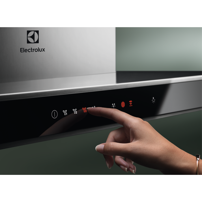 Egy kéz megnyom egy gombot egy fekete és ezüst páraelszívón, az Electrolux logója látható.