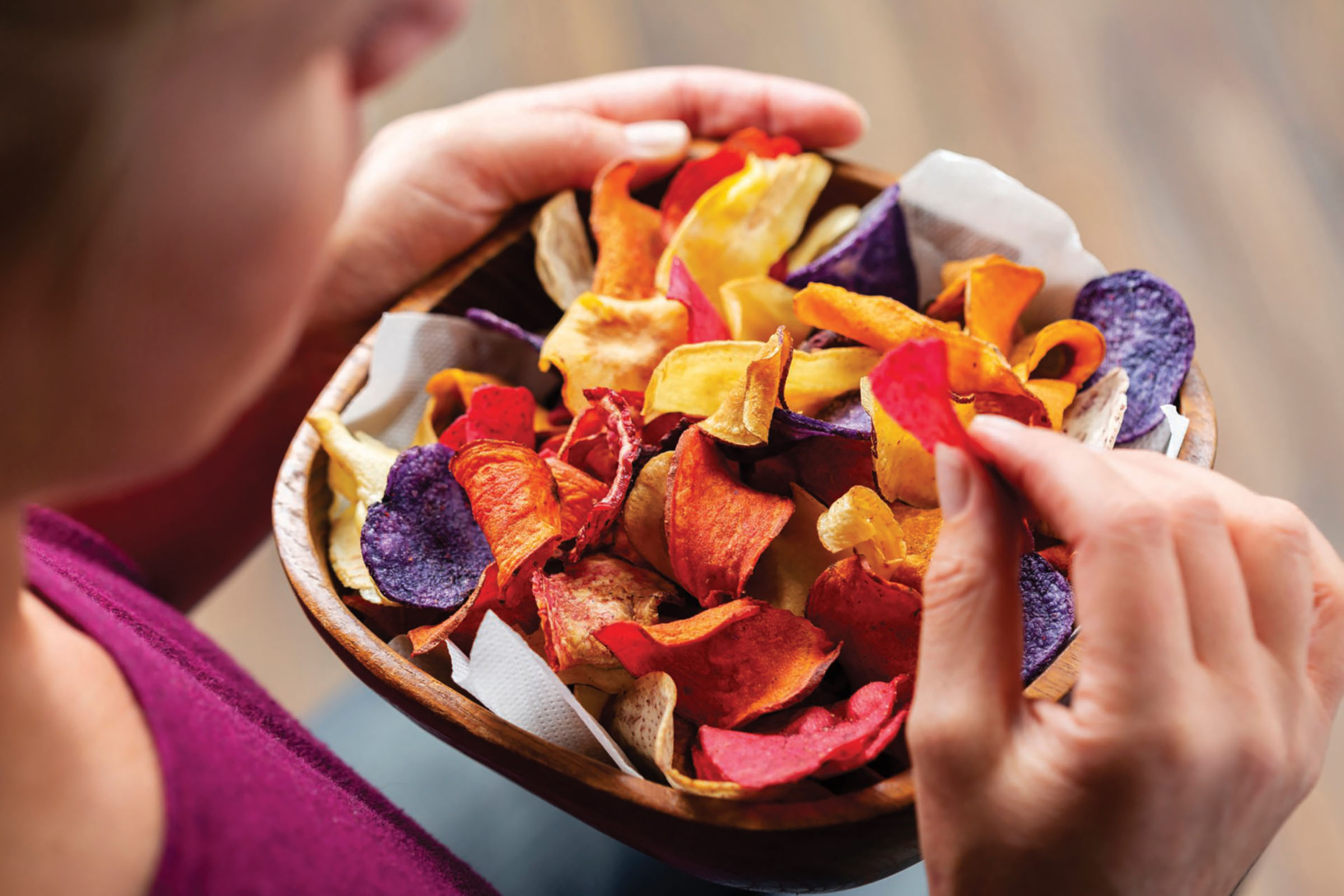Person hält Schüssel mit bunten Gemüsechips. Verschiedene Chips in der Schüssel.