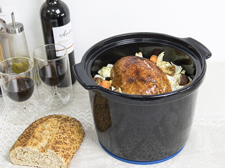 Asado en una olla negra con verduras, pan, copas de vino y una botella de vino. Una comida completa está lista.
