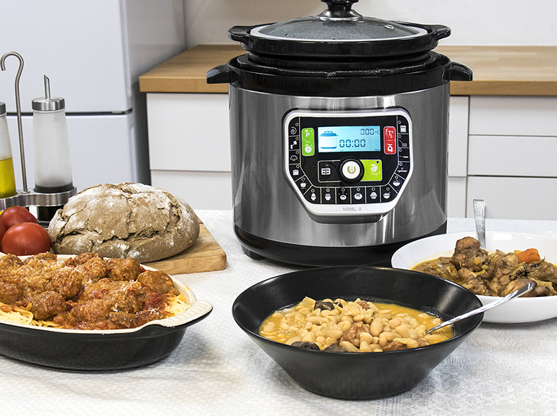 Una olla a presión con varios platos como pasta, guiso y frijoles. También hay una hogaza de pan y tomates en la mesa.