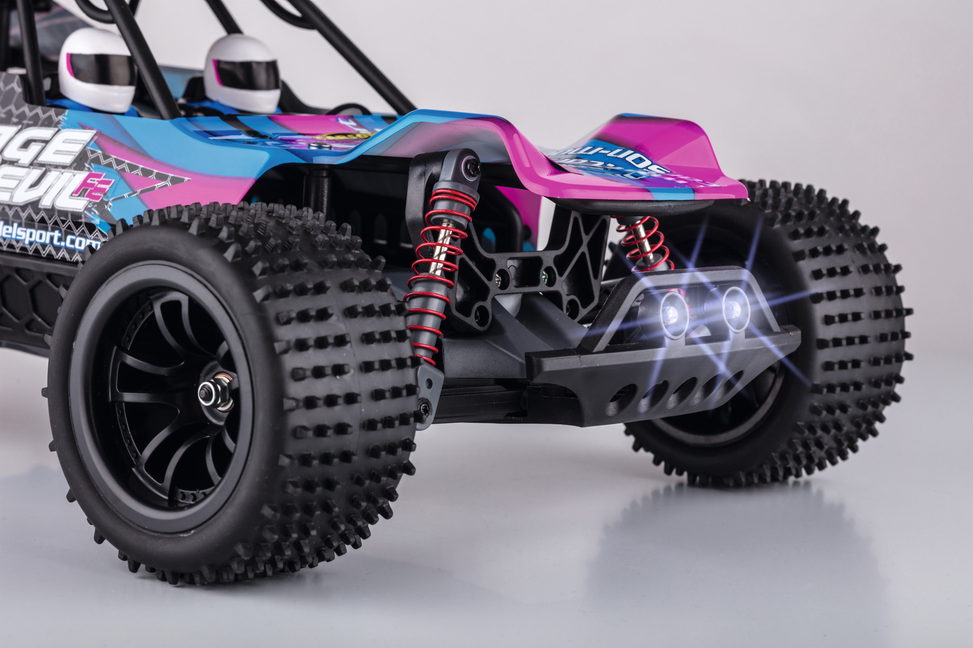 Nahaufnahme eines blau-rosa Spielzeugautos mit schwarzen Rädern und zwei kleinen Helmen.