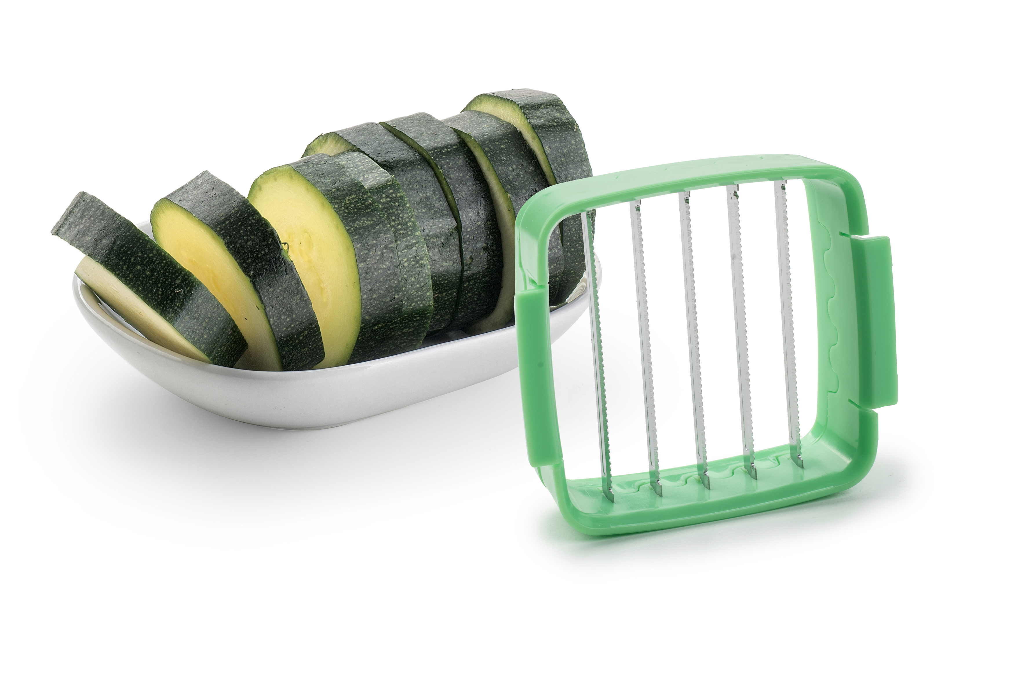 In Scheiben geschnittene Zucchini auf einem weißen Teller neben einem grünen Schneider.