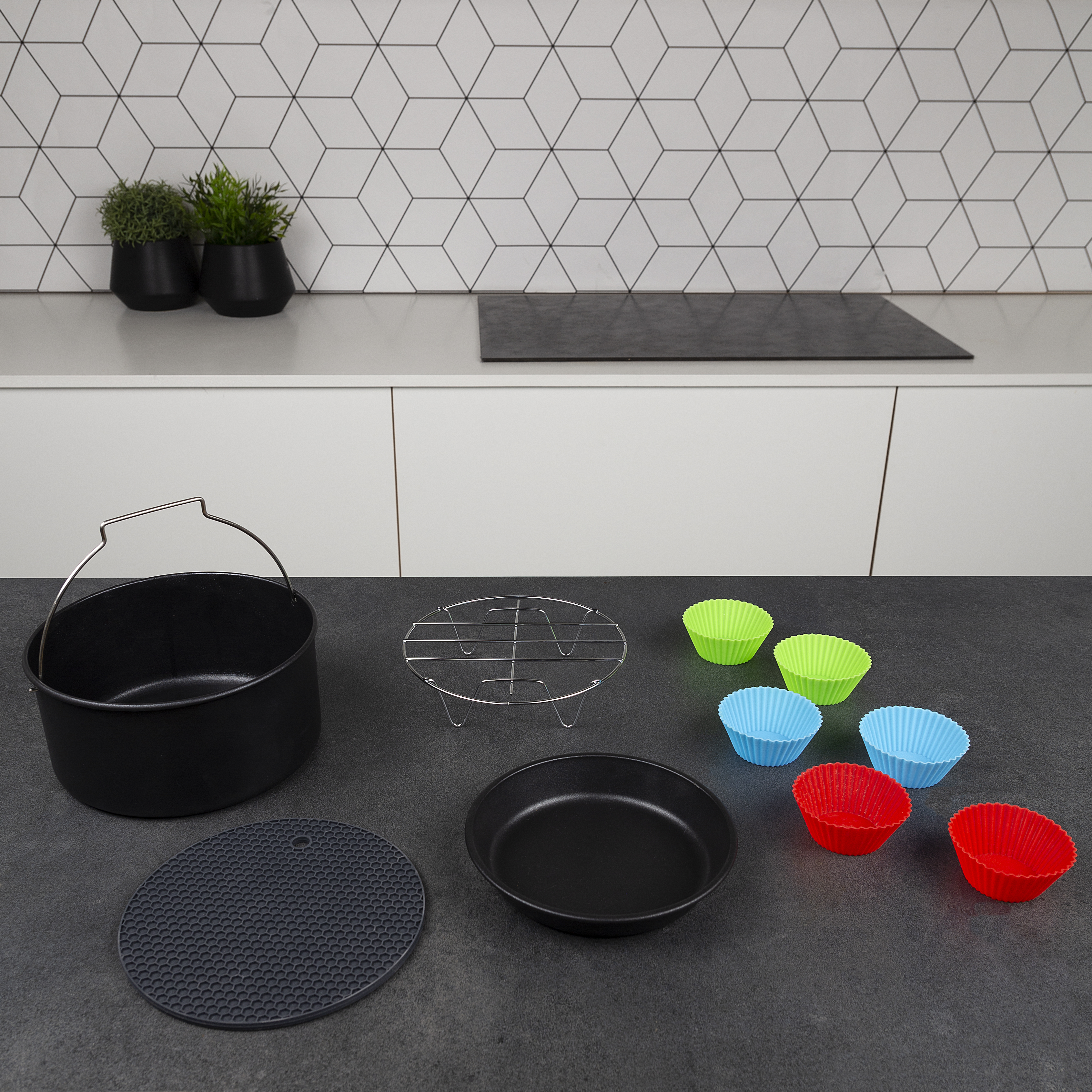 Air fryer accessories: a black pan, rack, silicone cups, and mat on a countertop.