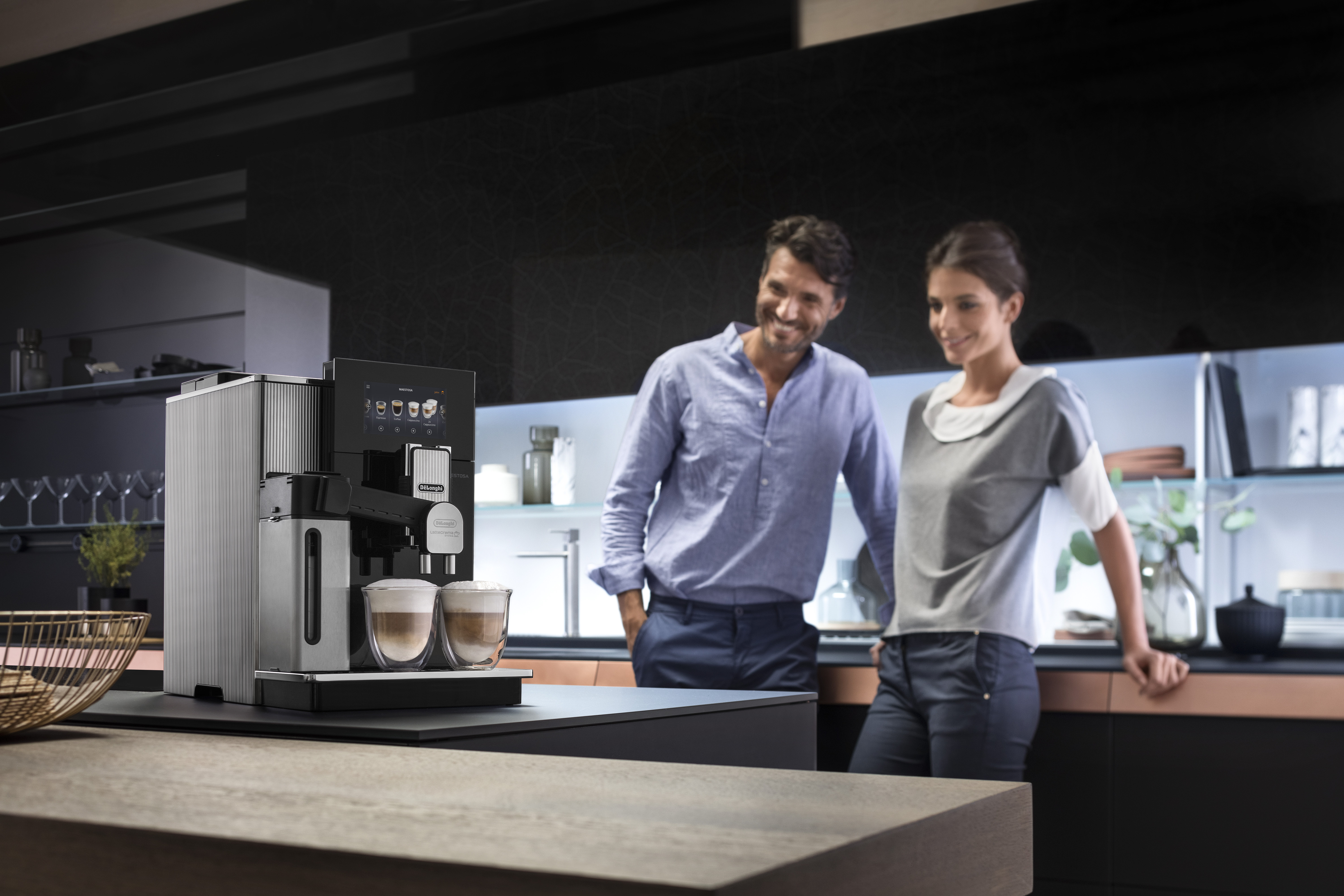 Ein Paar steht in einer modernen Küche neben einer silbernen Kaffeemaschine.