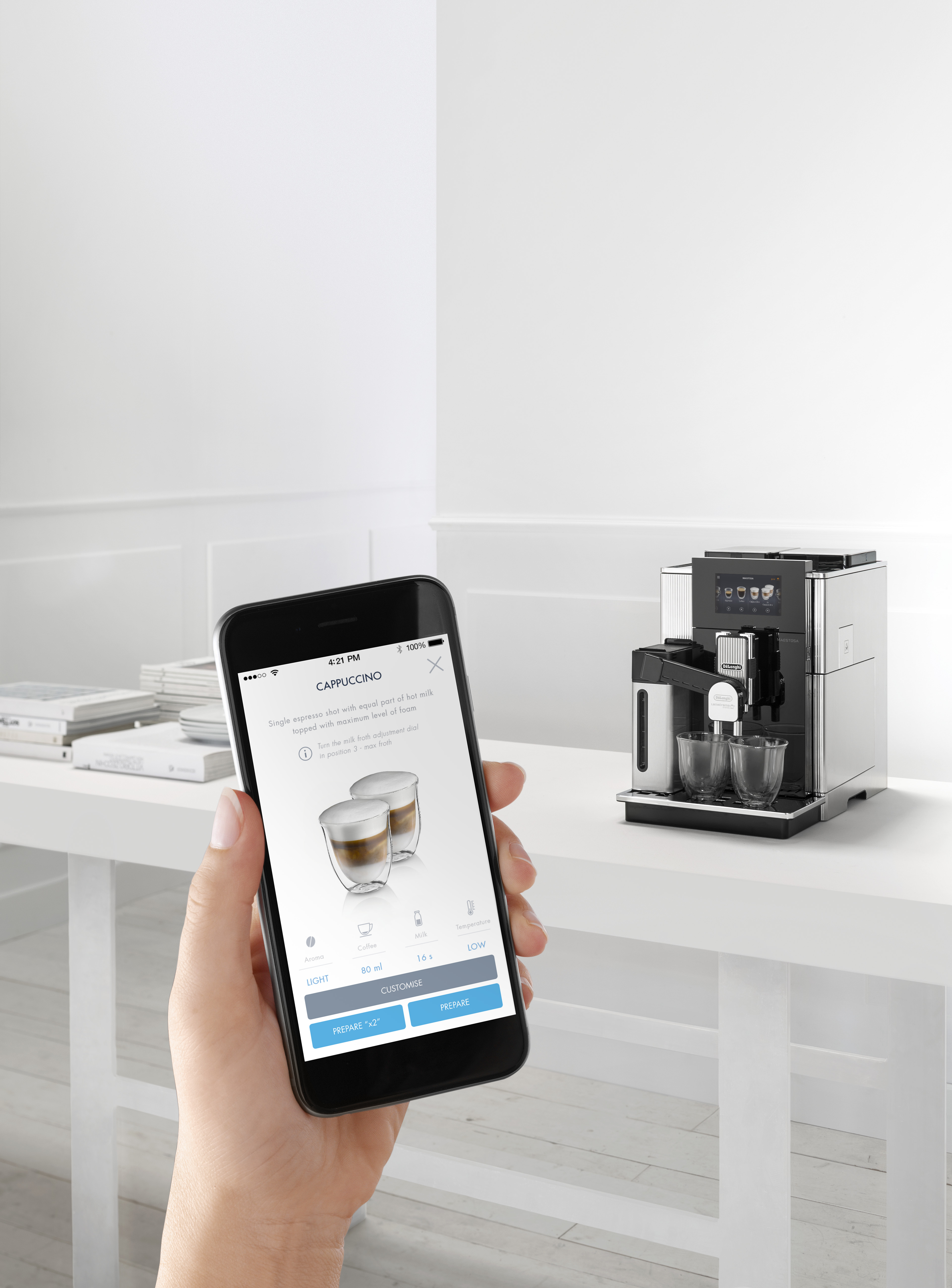 Eine Hand, die ein Telefon mit App-Oberfläche hält, neben einer Kaffeemaschine.