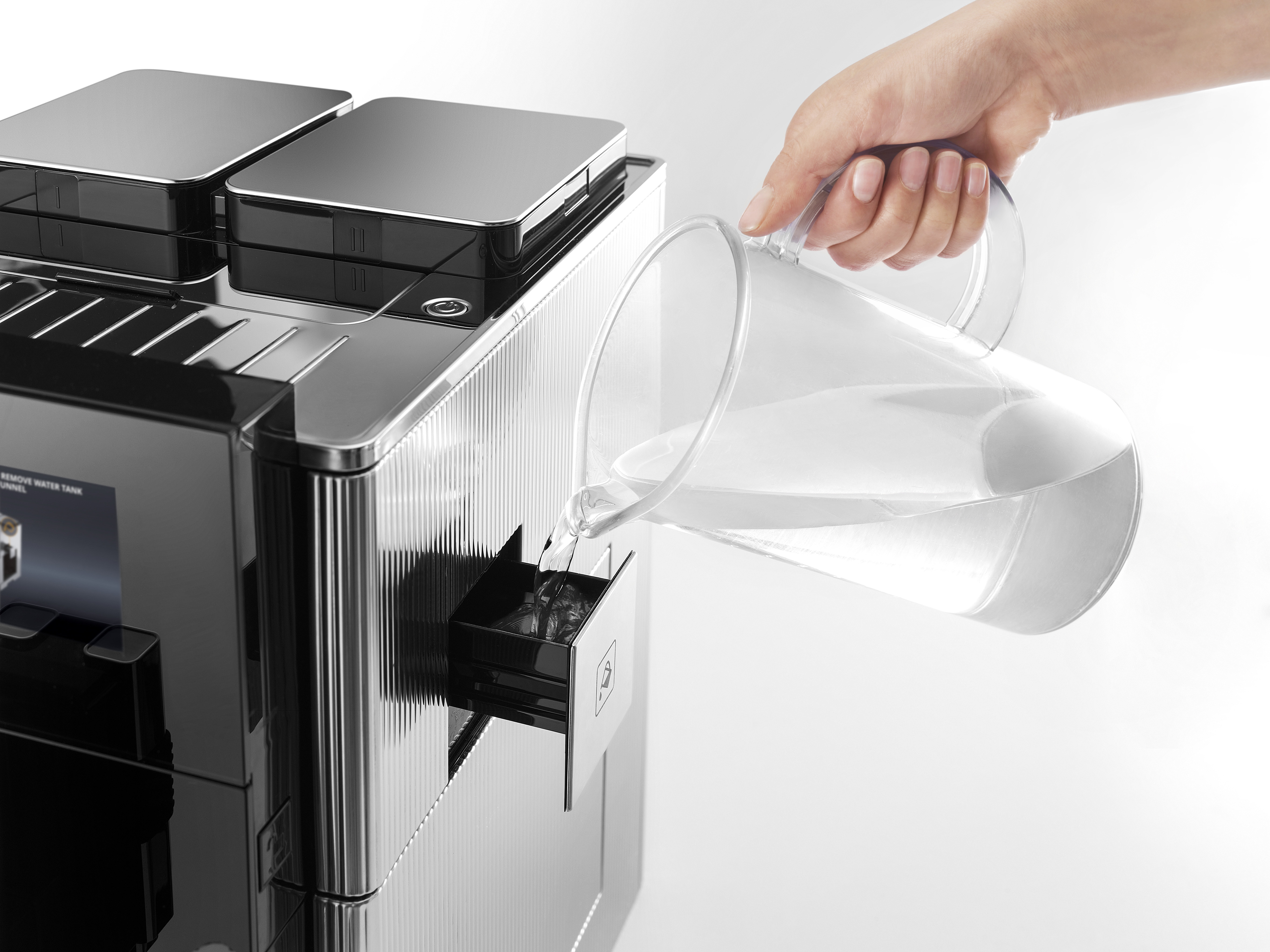 Eine Person gießt Wasser aus einem Krug in den Wassertank einer schwarz-silbernen Kaffeemaschine.