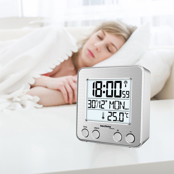 Silberne Digitaluhr auf Tisch neben schlafender Frau.