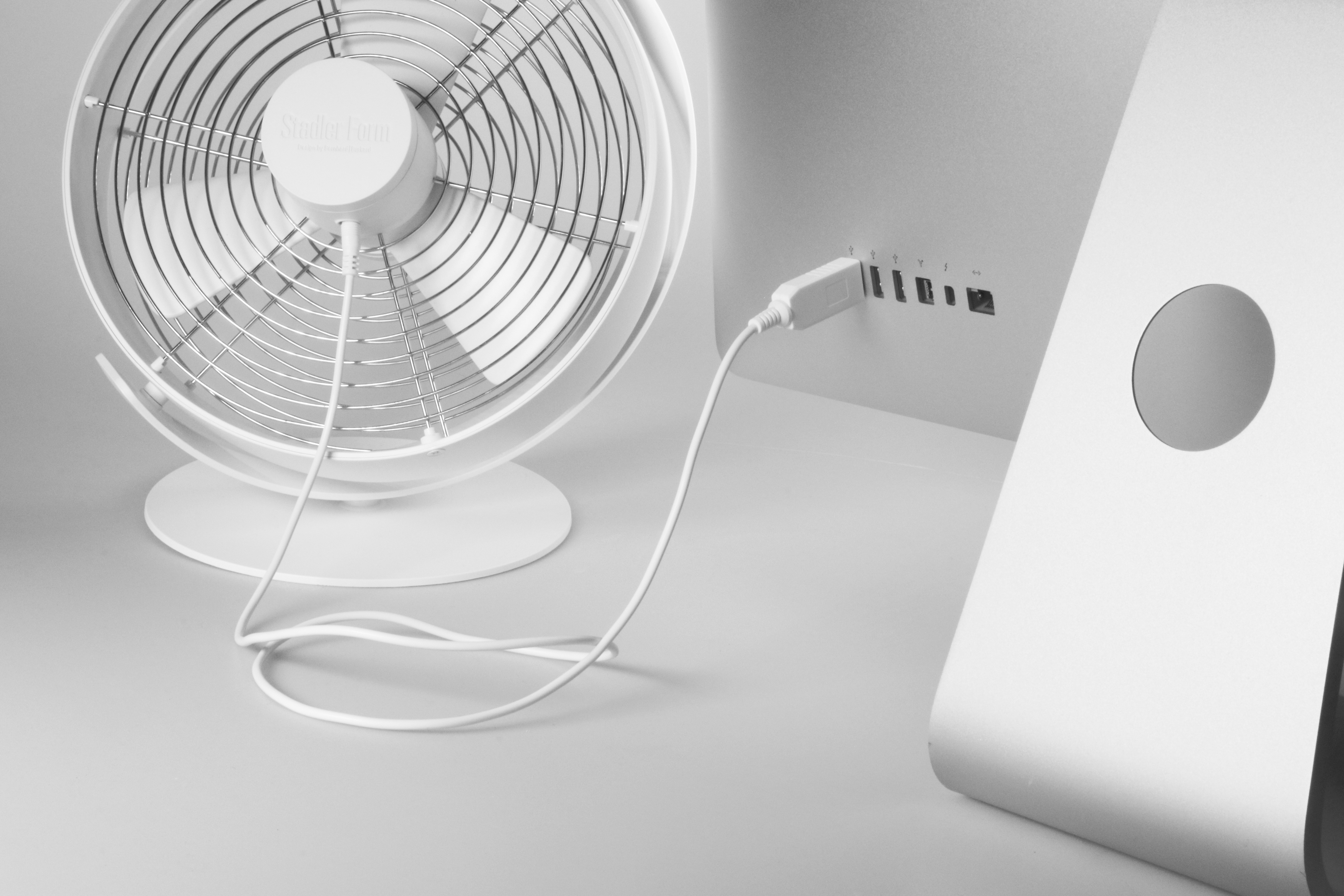 Weißer Ventilator, der mit einem Computer verbunden ist. Ventilator links, Computer rechts. Kabel verbindet.