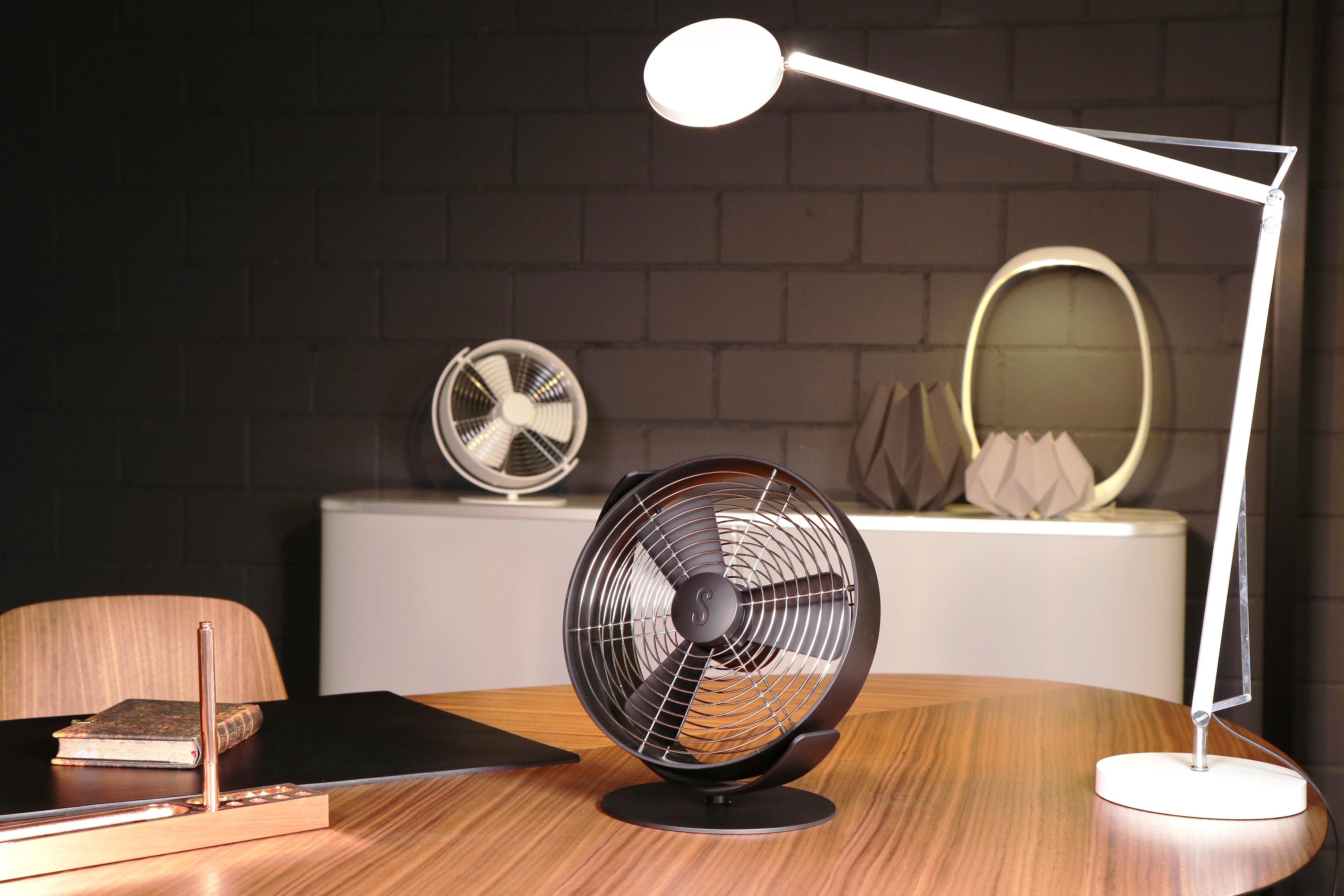 Modernes Büro-Setup mit Ventilatoren und Lampe. Holzschreibtisch und schwarze Wand.