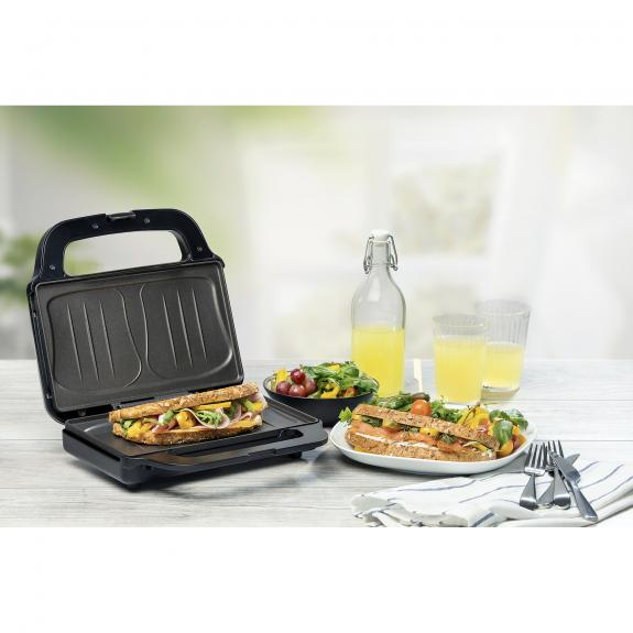 Sandwiches in a sandwich maker, with a side of salad and juice. The table is wooden.