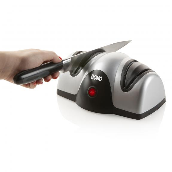 Een persoon gebruikt een messenslijper, met een zilver en zwart ontwerp, op een wit oppervlak.
