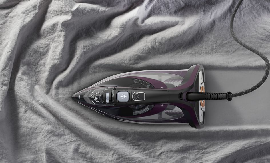 An iron on a grey sheet. It is black and purple with the cord attached.