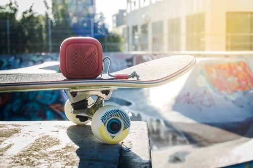 Altavoz portátil rojo sobre una patineta. La patineta está en una rampa de parque de patinaje.