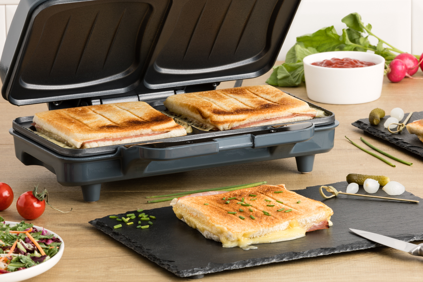 Sandwiches being made with a panini press, with side dishes.