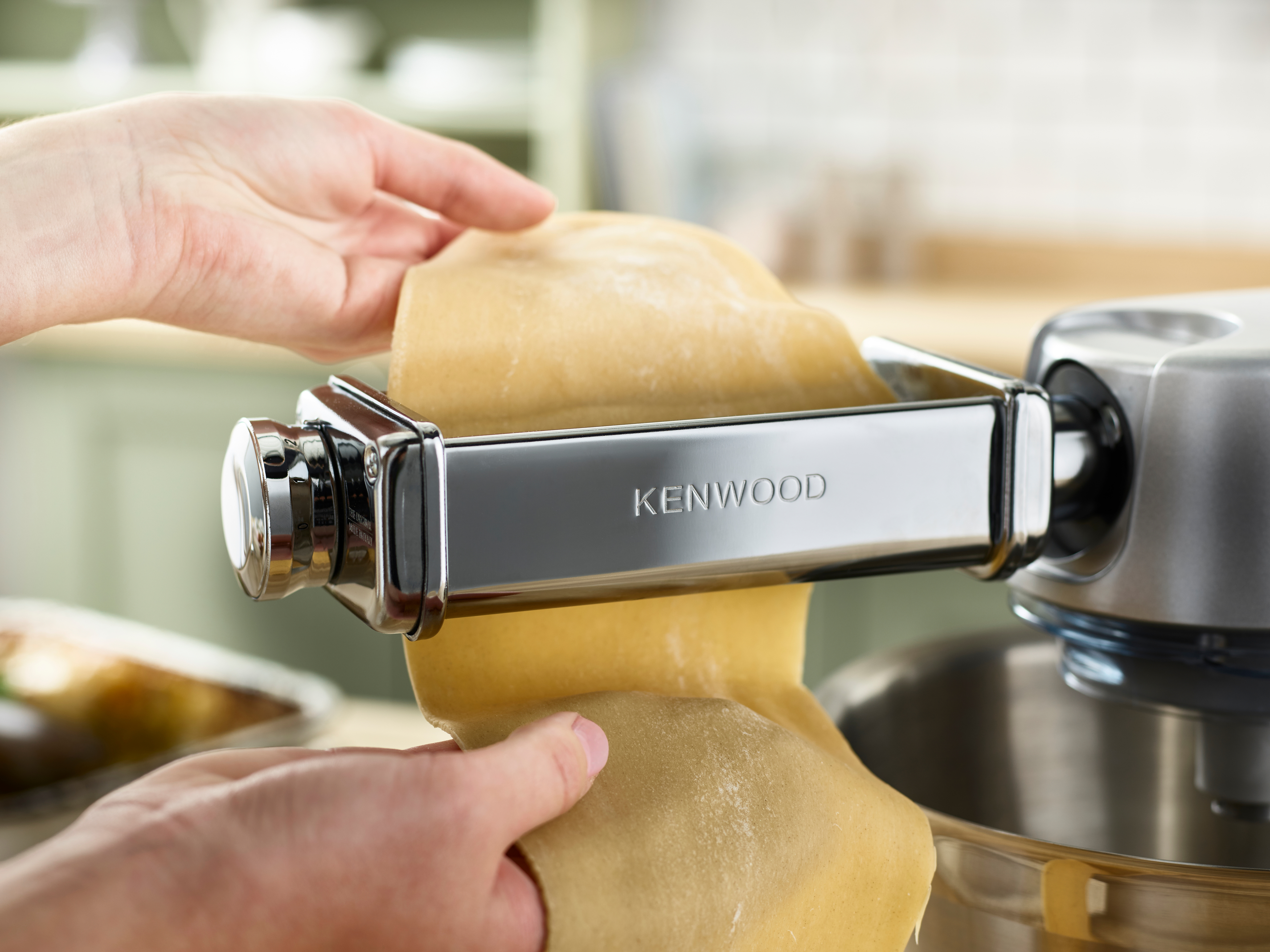Hände, die eine Kenwood-Nudelmaschine benutzen und frischen Teig ausrollen.