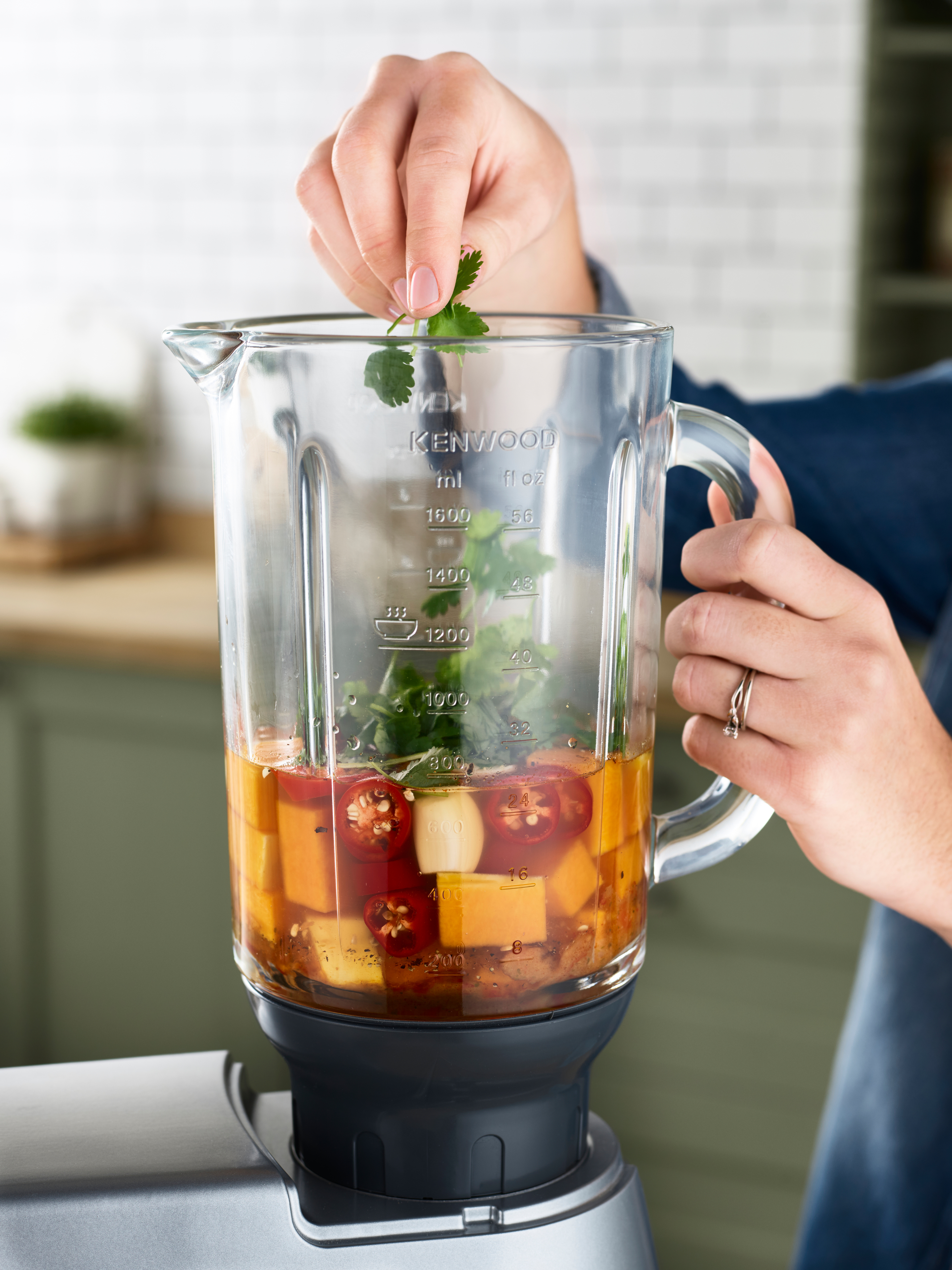 Eine Person gibt Koriander in einen Mixer mit Zutaten für ein Rezept.