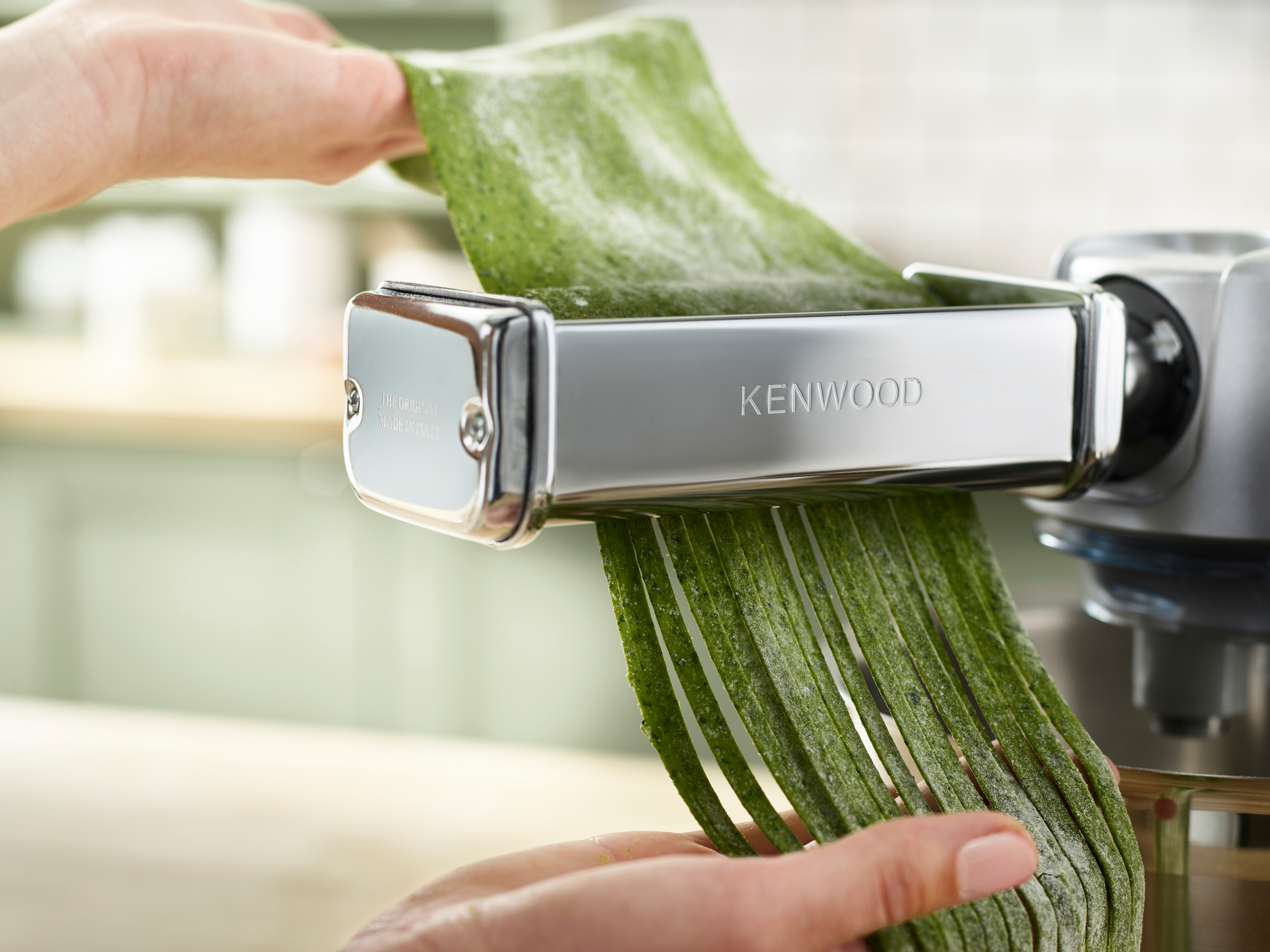 Hände benutzen Kenwood-Nudelmaschine, um grüne Nudelstreifen zu erzeugen.