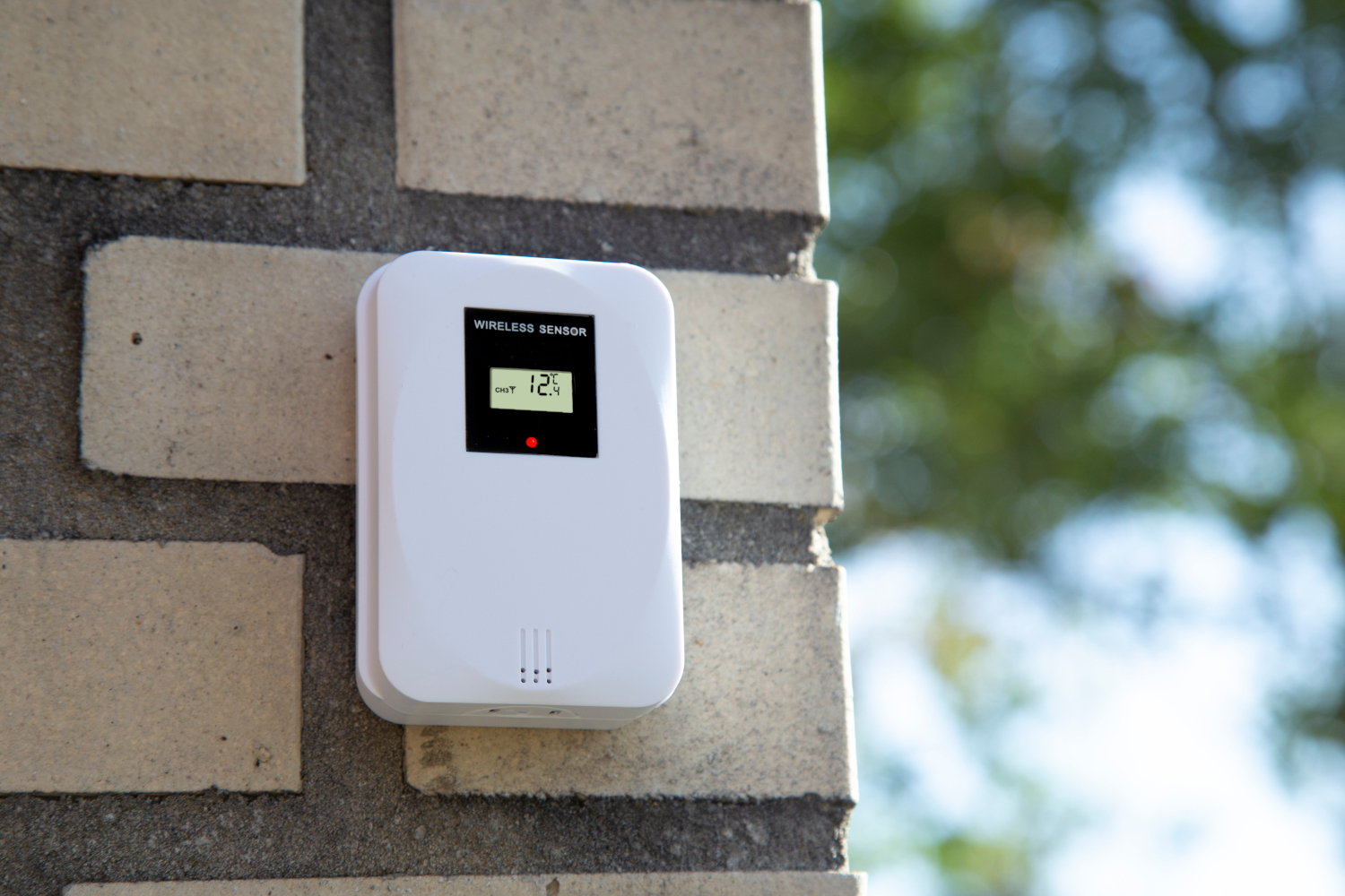 A white wireless sensor mounted on a brick wall. Displays temperature of 12 degrees.
