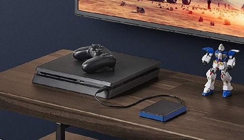Una consola Playstation 4 negra con un mando y un disco duro móvil sobre una mesa de madera.