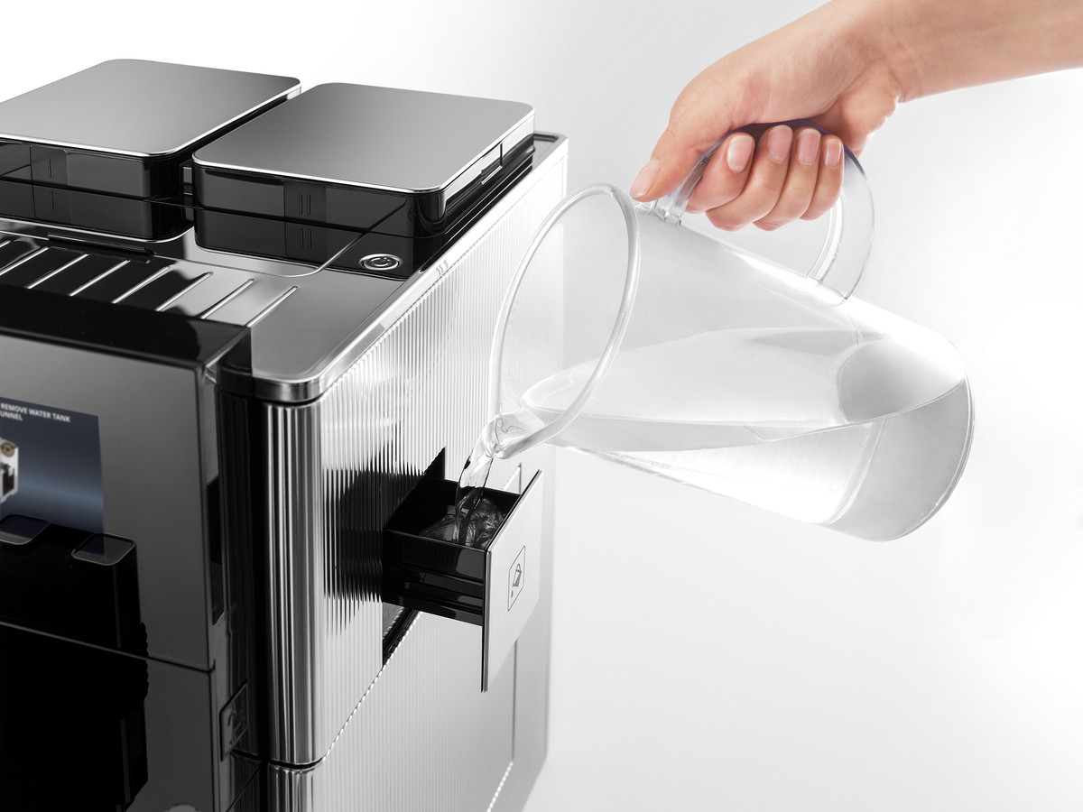 Schwarz-silberne Kaffeemaschine und eine Hand, die Wasser hineingießt.